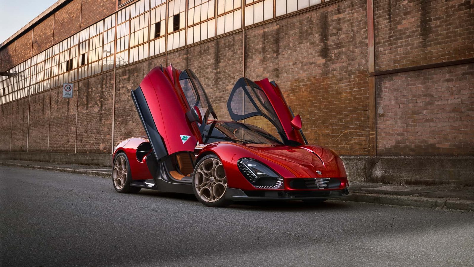Um elegante carro esportivo Alfa Romeo vermelho com portas que abrem verticalmente está estacionado em uma rua ao lado de um prédio de tijolos. Este 33 Stradale combina artisticamente uma obra-prima de design moderno e aerodinâmico com rodas grandes. | Velocidade5.cv