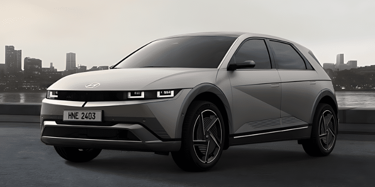 Um SUV prateado, a escolha certa para um estilo de vida urbano moderno, está estacionado perto de uma orla com um horizonte da cidade ao fundo. Suas linhas angulares e faróis distintos complementam seu design elegante, enquanto a placa "HNE 2403" se destaca sob o céu nublado. | Velocidade5.cv